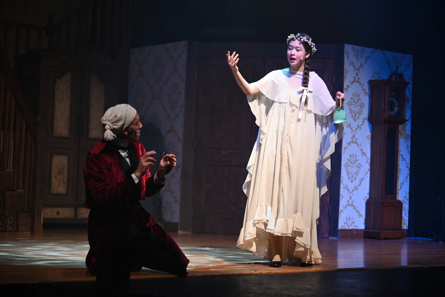 Scrooge kneels beside the Ghost of Christmas Past in the 2025 production.